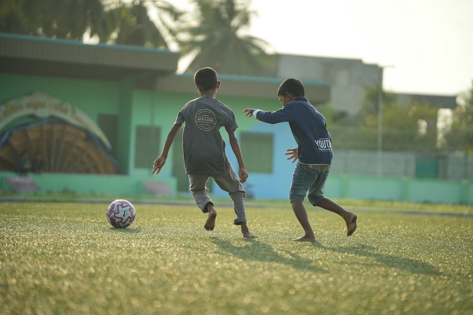 Deux enfants jouent au football sur une pelouse à la lumière du soir
